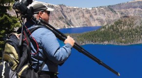 man-holding-camera-on-a-tripod-backpack-in-the-field